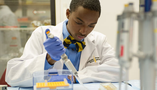 A student uses a pipette in a research laboratory on campus. He is wearing a lab coat that reads ‘Georgia Institue of Technology’ and sterile gloves.