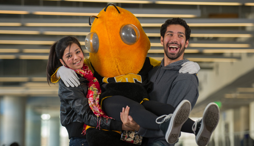 wo smiling students carry Buzz, Georgia Tech’s Yellow Jacket mascot.